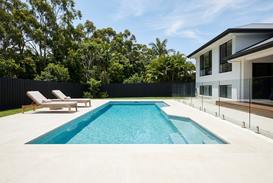 A pale liquid limestone surround around a backyard pool in summer